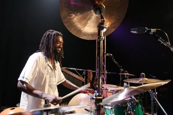 Adriano Adewale playing percussion smiling on stage