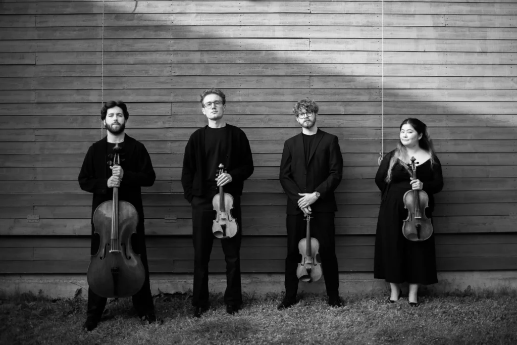 Elmore Quartet each with their instruments lined up against a wooden wall