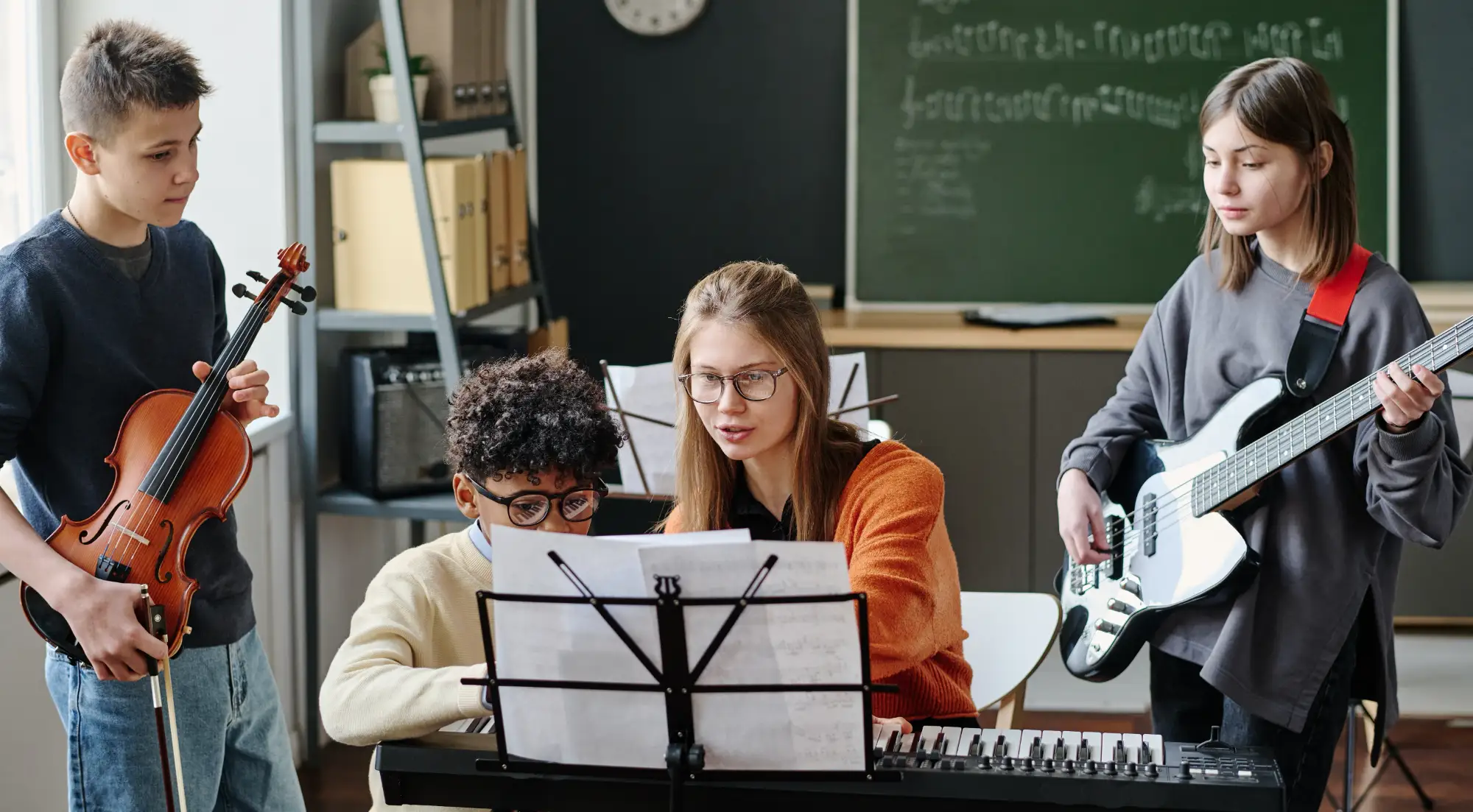 a teacher in a classroom helping a child to play an instrument with other children observing